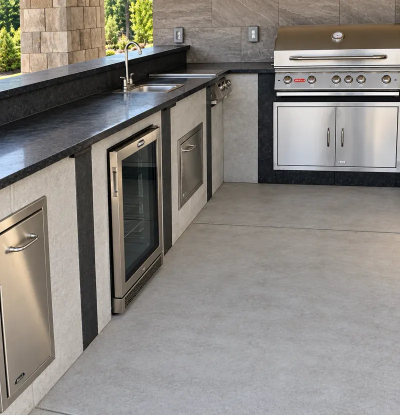 Outdoor kitchen with stone counters, built-in grill, sink, and refrigerator